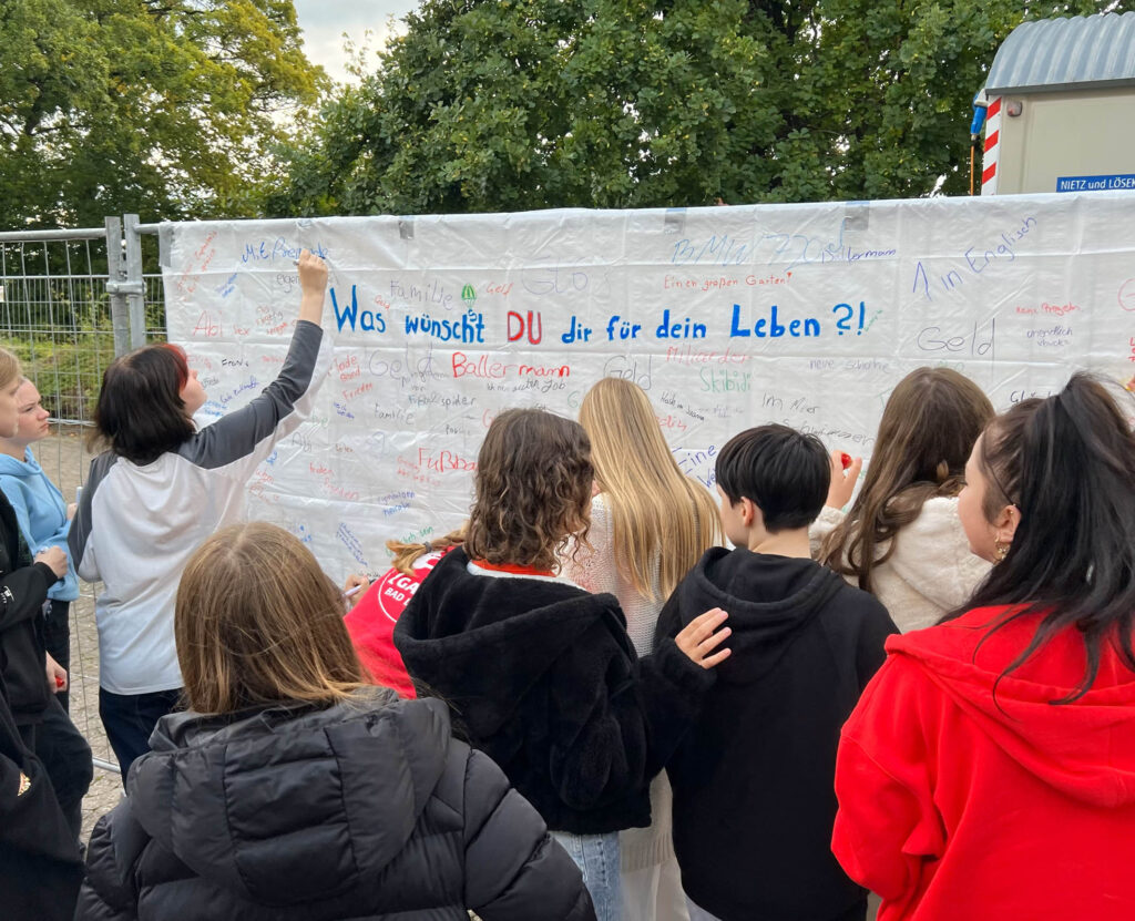 Junge Menschen schreiben bei einer Aktion der mobilen Jugendkirche Dome in Bad Driburg ihre Wünsche, Träume und Ziele auf eine Plane.